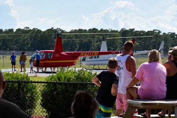 A landed red helicopter with people crowded around.