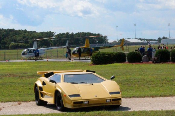 A couple of landed helicopters with a yellow Lamborghini in front.